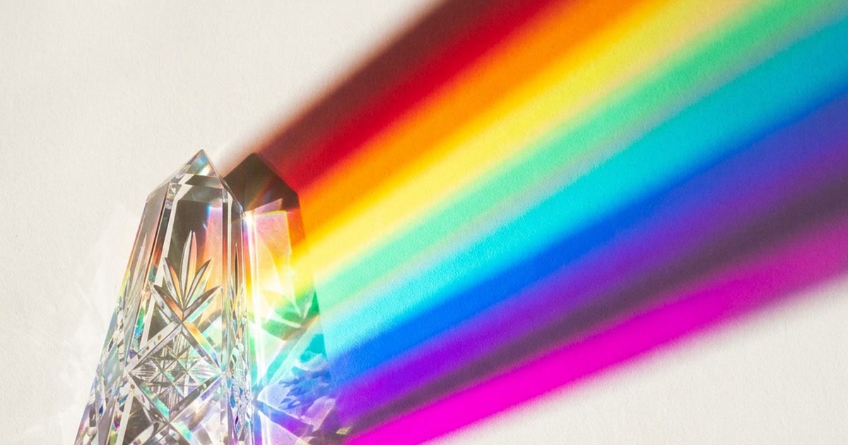 A cut crystal prism splitting a beam of light into a broad rainbow spectrum against white