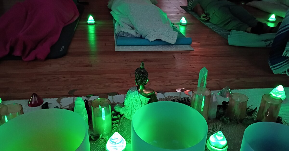 Crystal singing bowls and crystal points lit bright green in a dim room with mats and blankets laid out
