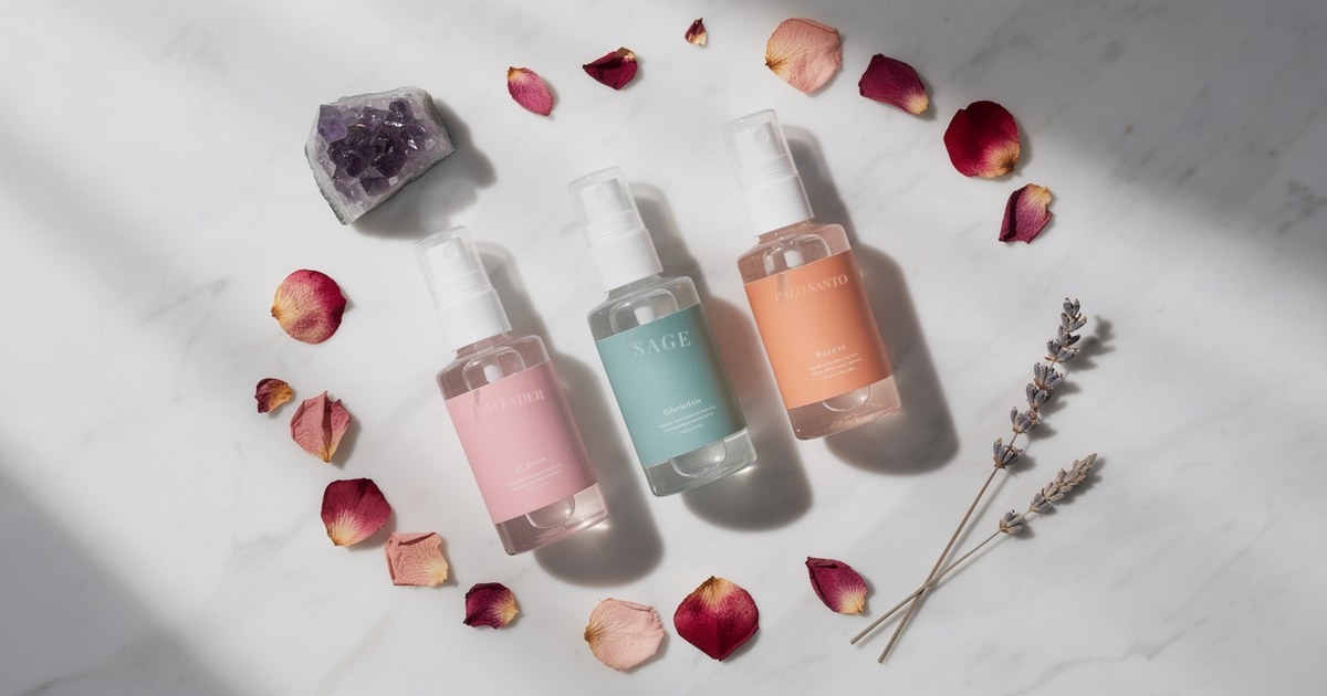 Three pump bottles in pink, teal and peach on white marble, encircled by rose petals, dried lavender stems and a raw amethyst cluster