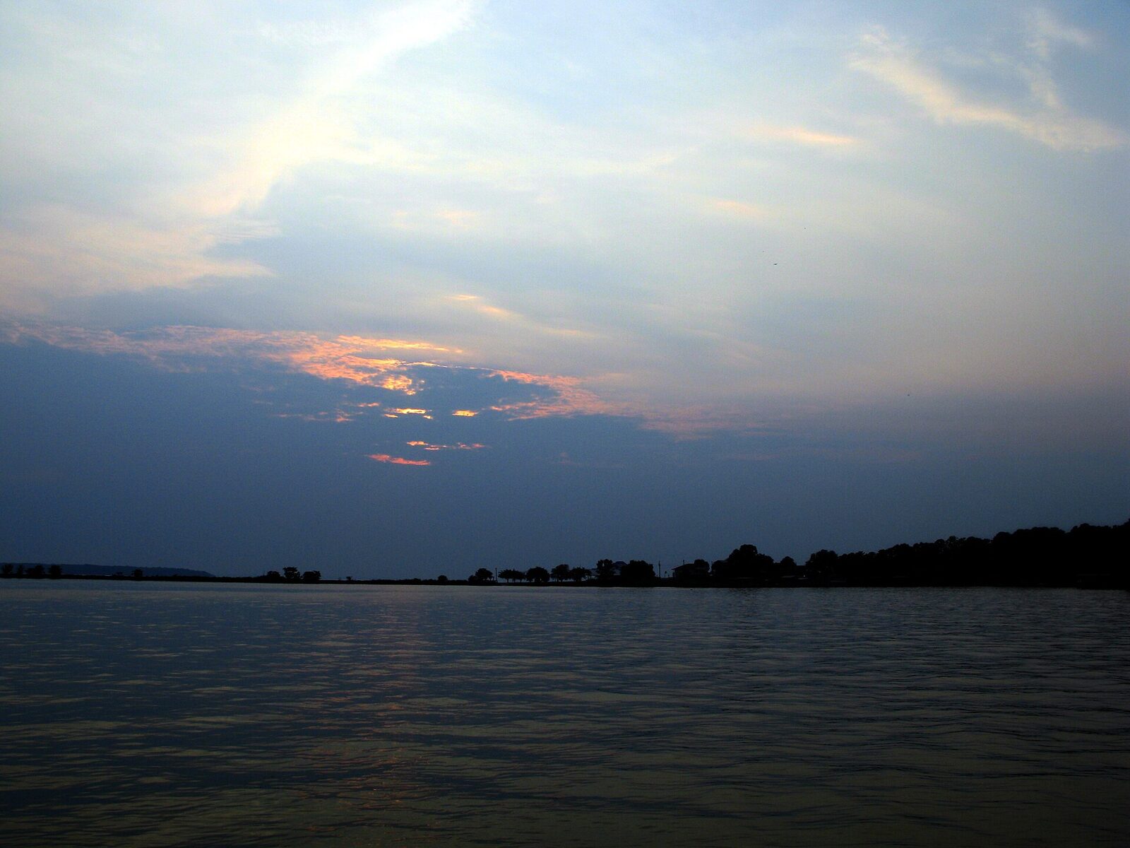 Still water under a pale sky at dawn, with low soft clouds along the horizon
