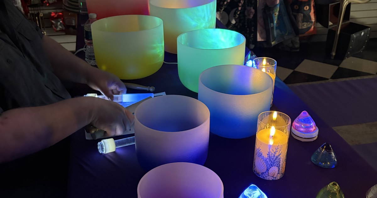 Frosted crystal singing bowls lit in blue, green and violet on a dark table with candles and small crystal points
